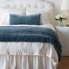 Carmen Throw Pillow | Mineral | Carmen 16x36 pillow and throw blanket in mineral, shown on an otherwise all white, neatly made bed - foot of bed angle.