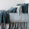 Carmen Throw Pillow | Mineral | Silk velvet throw pillows with petite ruffle on a monochromatic, neatly made bed with matching accessory pieces - side view.