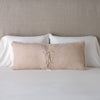 Carmen Throw Pillow | Pearl | Silk velvet lumbar pillow with petite ruffle leaning upright and backwards against neutral bedding and headboard, showcaseing the silk charmeuse tie closures.