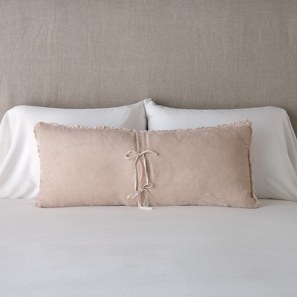Carmen Throw Pillow | Pearl | Silk velvet lumbar pillow with petite ruffle leaning upright and backwards against neutral bedding and headboard, showcaseing the silk charmeuse tie closures.