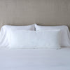 Carmen Throw Pillow | White | Silk velvet lumbar pillow with petite ruffle, leaning upright against neutral bedding and headboard.