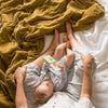Carmen Blanket | Mother and baby sitting on rumpled honeycomb Carmen throw blanket and white linen - overhead view.