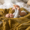 Carmen Blanket | Baby laying playfully, looking at the camera, on rumpled honeycomb Carmen throw blanket - side view.
