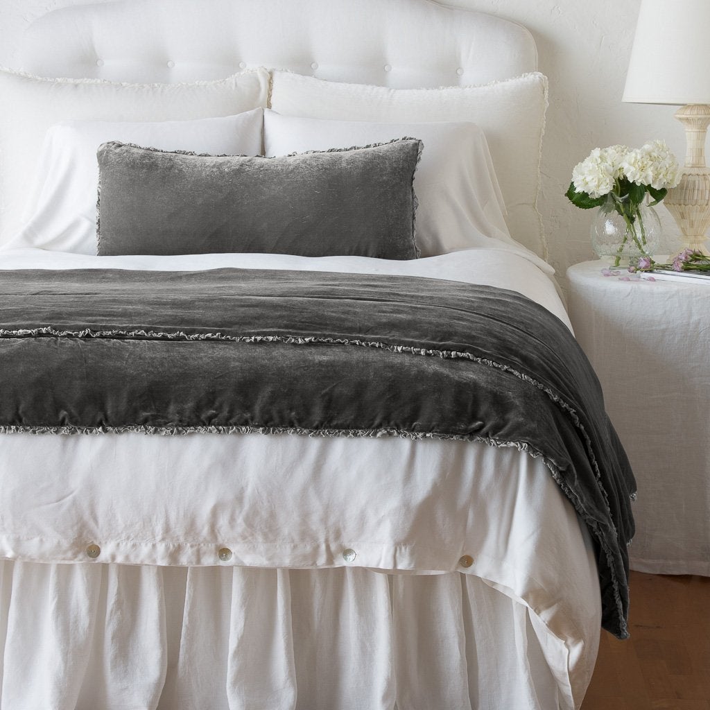 Carmen Blanket | Fog | Carmen throw blanket and lumbar pillow in fog draped at the end of a white bed - end of bed view.
