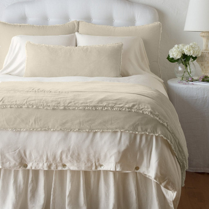 Carmen Blanket | Parchment | Silk velvet throw blanket with petite ruffle draped at the end of a monochromatic bed - end of bed view.
