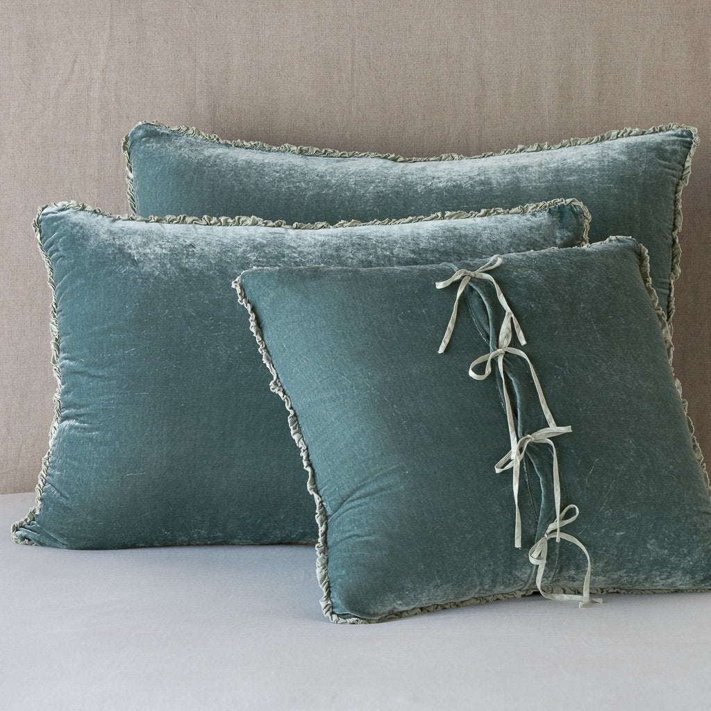 Three carmen shams in eucalyptus leaning upright against a neutral headboard. The front sham is backwards, showcasing the charmeuse tie closures.