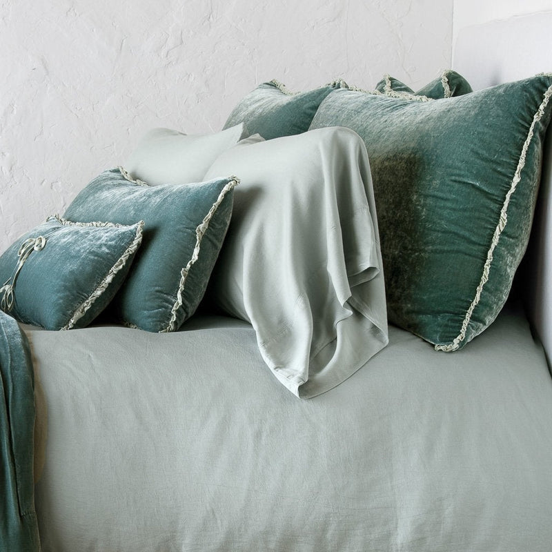 Carmen Sham | Eucalyptus | Silk velvet shams with a petite ruffle on monochromatic bed, leaning upright behind sleeping and throw pillows - side view.