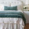 Carmen Sham | Eucalyptus | Silk velvet shams with a petite ruffle on a white bed, stacked behind sleeping and throw pillows - view from end of bed.