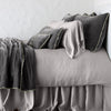 Carmen shams in fog on monochromatic bed, leaning upright behind sleeping and throw pillows - side view.
