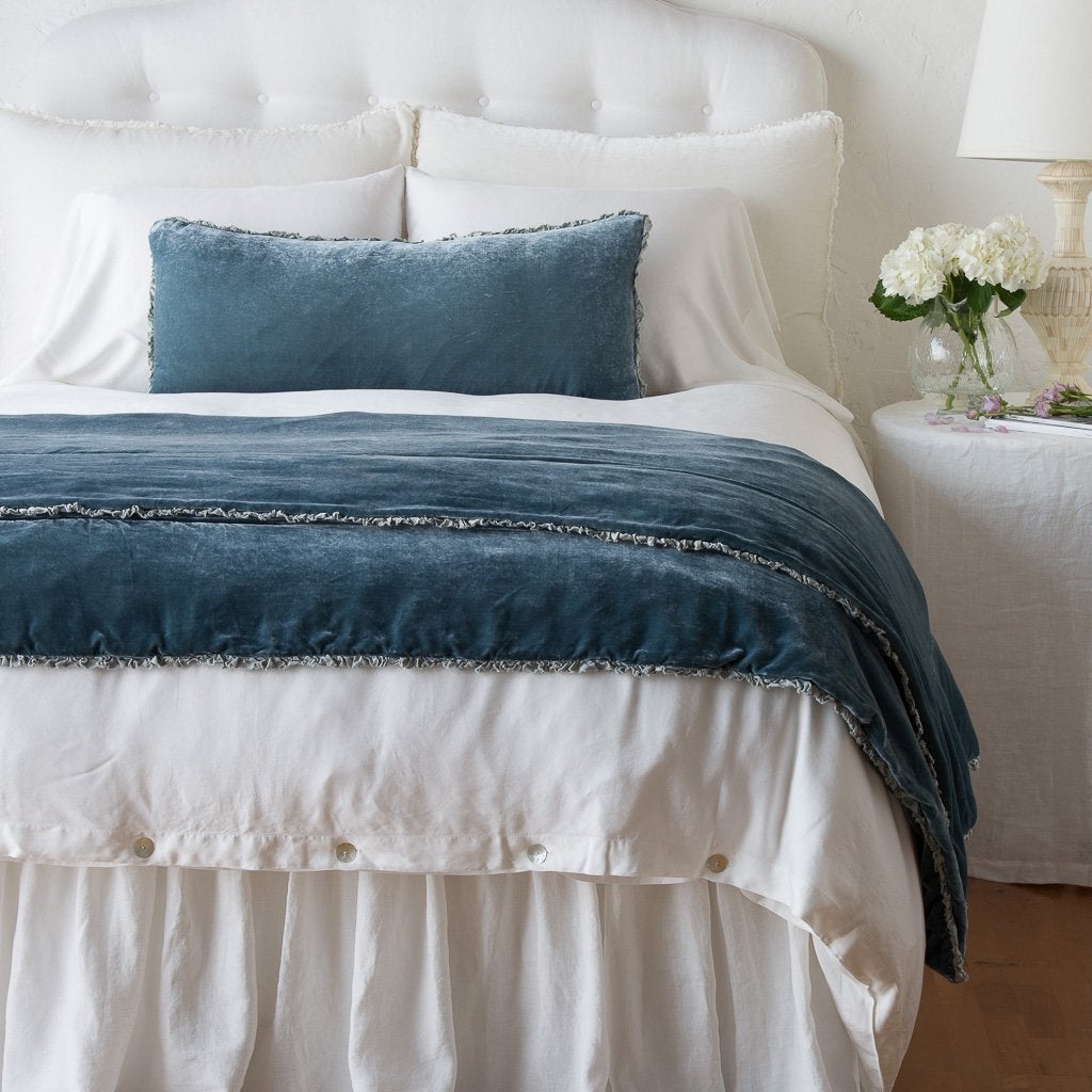 Carmen Sham | Mineral | Silk velvet shams with a petite ruffle on a white bed, stacked behind sleeping and throw pillows - view from end of bed.