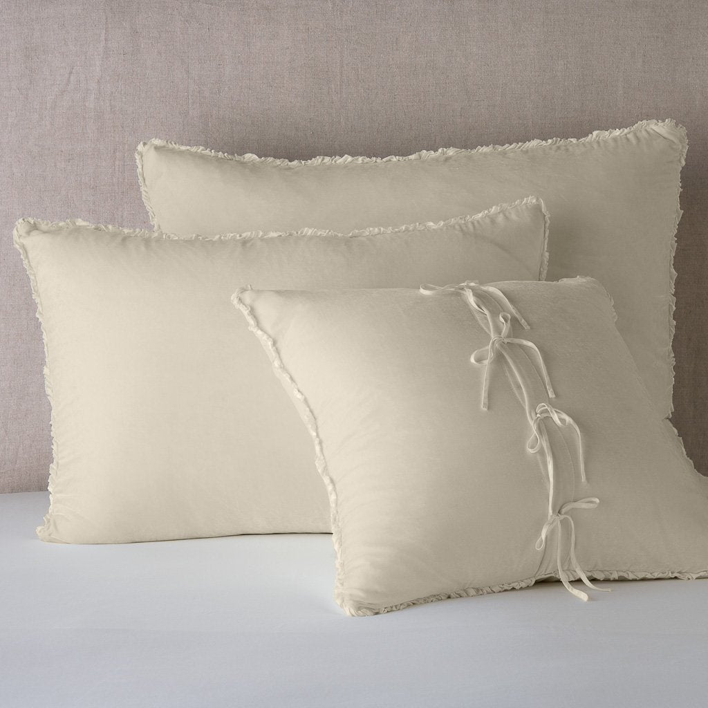 Carmen Sham | Parchment | Silk velvet  shams with a petite ruffle leaning upright against a neutral headboard. The front sham is backwards, showcasing the charmeuse tie closures.