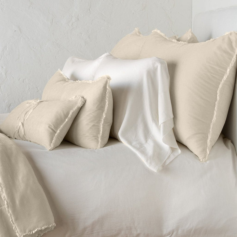 Carmen Sham | Parchment | Silk velvet shams with a petite ruffle on monochromatic bed, leaning upright behind sleeping and throw pillows - side view.