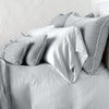 Carmen shams in sterling on monochromatic bed, leaning upright behind sleeping and throw pillows. Close-up side view showcases the charmeuse petite raw-edge ruffle.