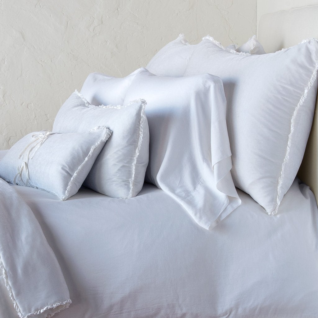 Carmen Sham | White | Silk velvet shams with a petite ruffle on monochromatic bed, leaning upright behind sleeping and throw pillows - side view.