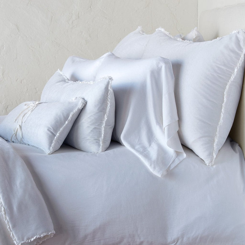 Carmen Sham | White | Silk velvet shams with a petite ruffle on monochromatic bed, leaning upright behind sleeping and throw pillows - side view.