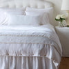 Carmen Sham | White | Silk velvet shams with a petite ruffle on a monochromatic bed, stacked behind sleeping and throw pillows - view from end of bed.