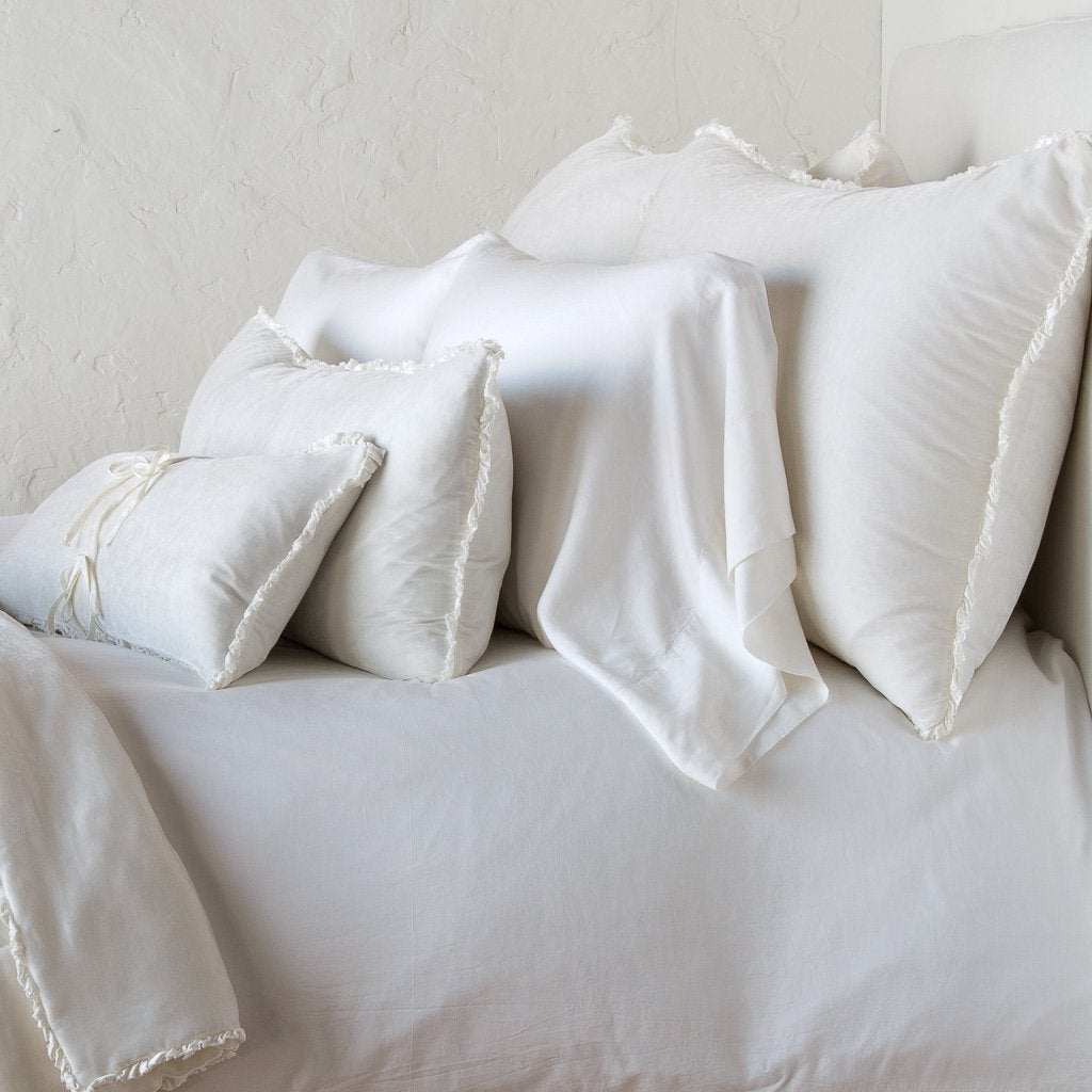 Carmen Sham | Winter White | Silk velvet shams with a petite ruffle on monochromatic bed, leaning upright behind sleeping and throw pillows - side view.