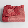 Cirillo Baby Blanket | Poppy | a folded quilted cotton sateen baby blanket with its corner folded down to show the trim contrast - shot against a white background.