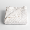 Cirillo Baby Blanket | Winter White | a folded quilted cotton sateen baby blanket with its corner folded down to show the trim contrast - shot against a white background.
