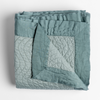 Cirillo Blanket | Eucalyptus | a folded quilted cotton sateen throw blanket with its corner folded down to show the trim contrast - shot against a white background.