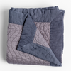 Cirillo Blanket | French Lavender | a folded quilted cotton sateen throw blanket with its corner folded down to show the trim contrast - shot against a white background.