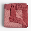 Cirillo Blanket | Poppy | a folded quilted cotton sateen throw blanket with its corner folded down to show the trim contrast - shot against a white background.