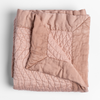 Cirillo Blanket | Rouge | a folded quilted cotton sateen throw blanket with its corner folded down to show the trim contrast - shot against a white background.