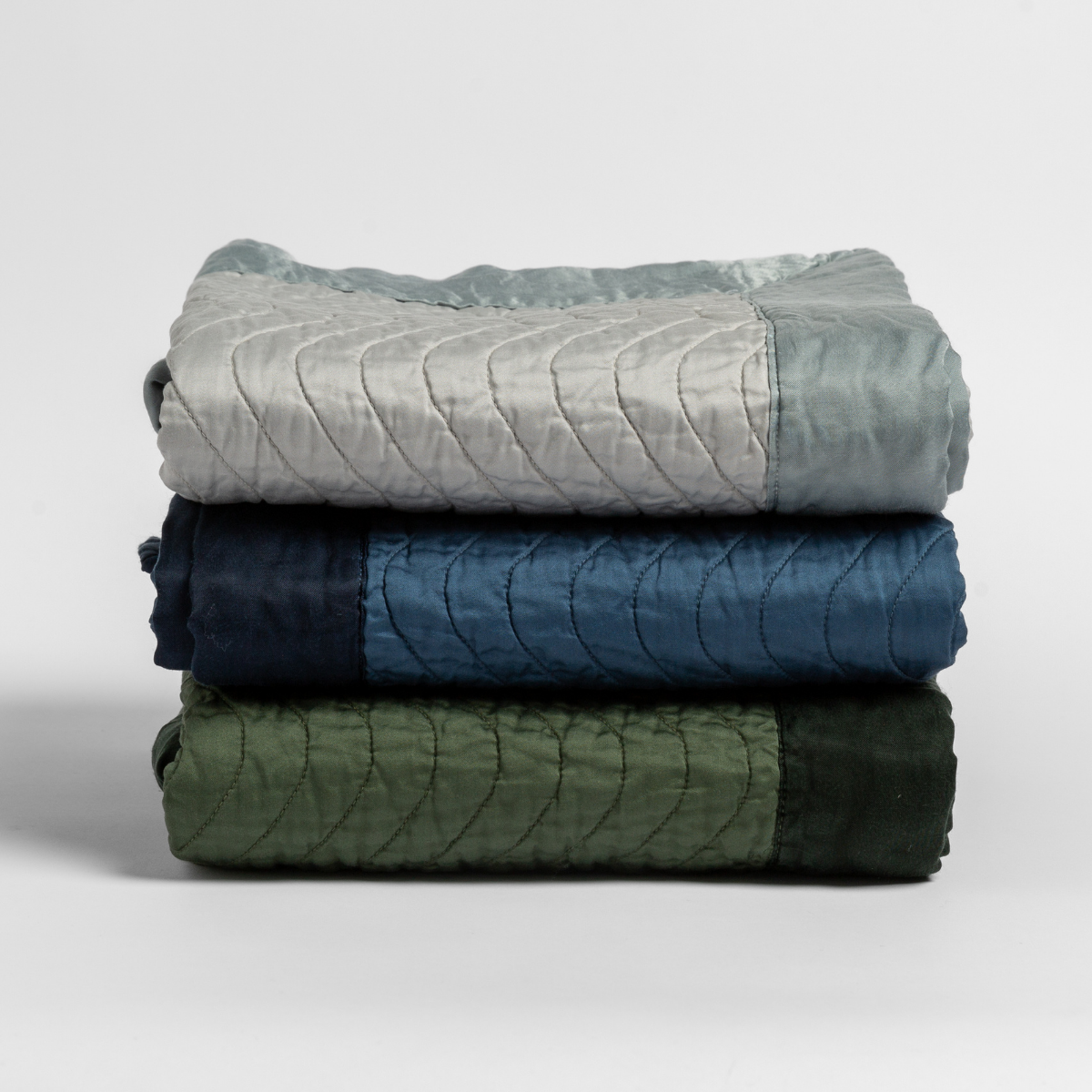 Cirillo Blanket | a stack of blankets in green and blue tones against a white background.