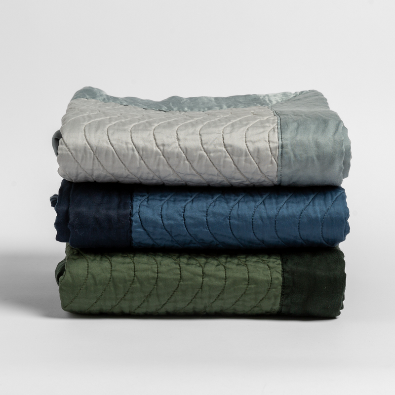 Cirillo Blanket | a stack of blankets in green and blue tones against a white background.