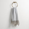 Frida Guest Towel | Cloud | Lace trimmed linen guest towel  draped through a decorative towel ring against a plain white background.