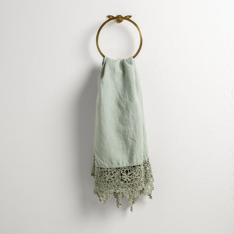 Frida Guest Towel | Eucalyptus | Lace trimmed linen guest towel  draped through a decorative towel ring against a plain white background.