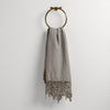 Frida Guest Towel | Mineral | Lace trimmed linen guest towel  draped through a decorative towel ring against a plain white background.