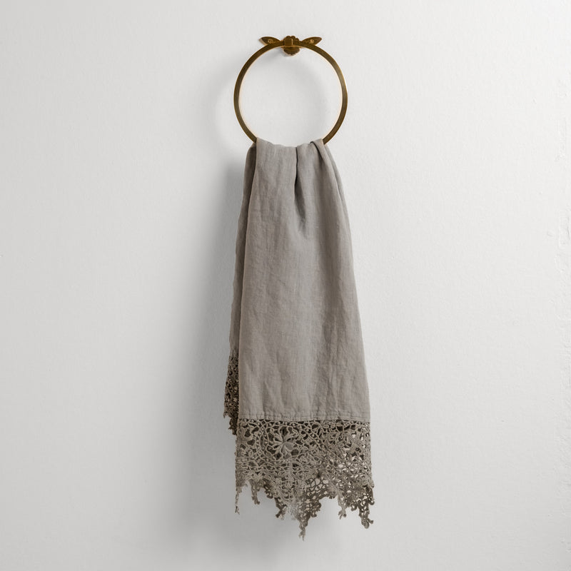 Frida Guest Towel | Mineral | Lace trimmed linen guest towel  draped through a decorative towel ring against a plain white background.