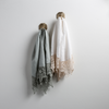 Two Frida guest towels, draped over decorative hooks against a white wall - eucalyptus and winter white