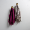 Two Frida guest towels, draped over decorative hooks against a white wall - fig and fog.