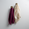 Two Frida guest towels, draped over decorative hooks against a white wall - fig and parchment.