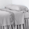Frida Flat Sheet | Fog | Lace trimmed linen flat sheet neattly folded back on a monochromatic linen bed - cropped three-quarter angle.