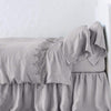 Frida Flat Sheet | Fog | Lace trimmed linen flat sheet folded back over monochromatic linen bed - side view.