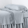 Frida flat sheet in cloud, neatly folded back on a monochromatic linen bed - cropped three-quarter angle.