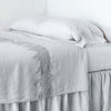 Frida Flat Sheet | Sterling | Lace trimmed linen flat sheet neattly folded back on a monochromatic linen bed - cropped three-quarter angle.