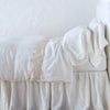 Frida Flat Sheet | Winter White | Lace trimmed linen flat sheet folded back over monochromatic linen bed - side view.