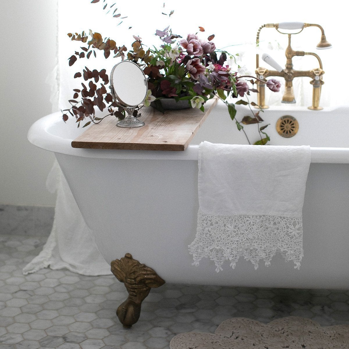 White | Frida guest towel draped over the edge of an antique tub, with copper accents and lavender and green floral bouquet.