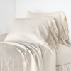 Frida Pillowcase (Single) | Parchment | Lace trimmed linen pillowcases leaning against a plain wall on a monochromatic bed - cropped three-quarter angle.