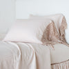 Frida Pillowcase (Single) | Frida pillowcases leaning against a plain wall on a monochromatic pearl bed - cropped three-quarter angle.