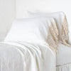 Frida Pillowcase (Single) | Winter White | Lace trimmed linen pillowcases leaning against a plain wall on a monochromatic bed - cropped three-quarter angle.