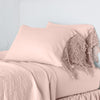 Frida Pillowcase (Single) | Rouge | Lace trimmed linen pillowcases leaning against a plain wall on a monochromatic bed - cropped three-quarter angle.
