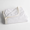 Harlow Baby Blanket | White | cotton velvet baby blanket trimmed with charmeuse, folded with a covern folded back to show trim contrast; shot overhead and at a slight angle against a white background.