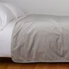 Harlow Blanket | Fog | Cotton velvet bed end sized blanket, draped on a white bed - side view.