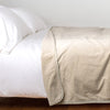 Harlow Blanket | Parchment | Cotton velvet blanket, draped on a white bed with corner folded back - side view.