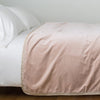 Harlow Blanket | Pearl | Cotton velvet bed end sized blanket, draped on a white bed - side view.